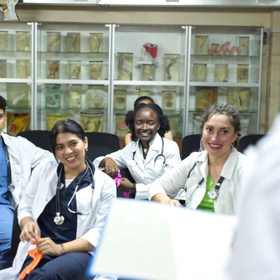 4 students in white lab coats smile and listen to someone speaking.