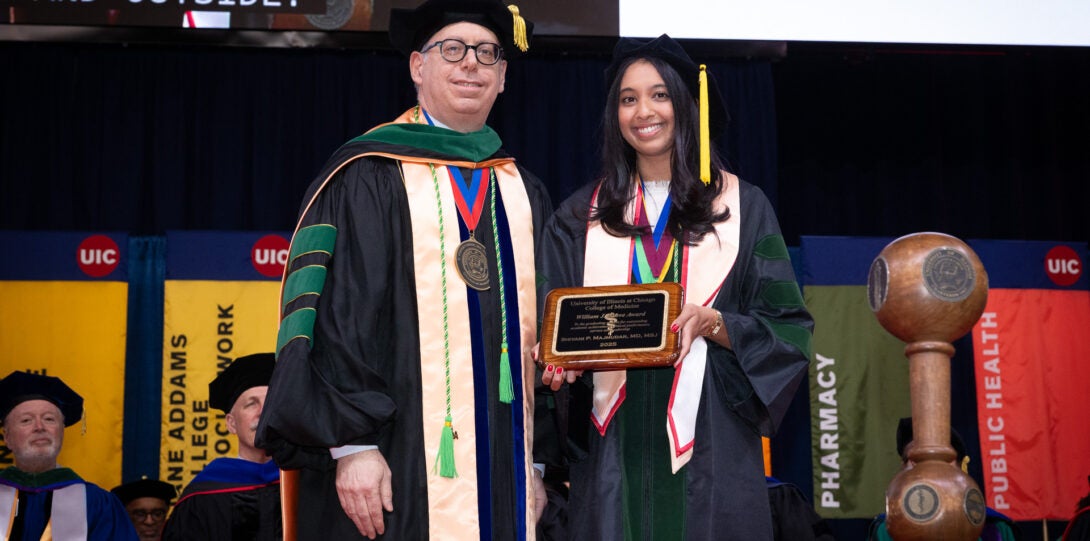 A student smiles with Dean Mark Rosenblatt holding their degree