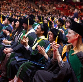 Students in caps and gowns applaud in their seats 