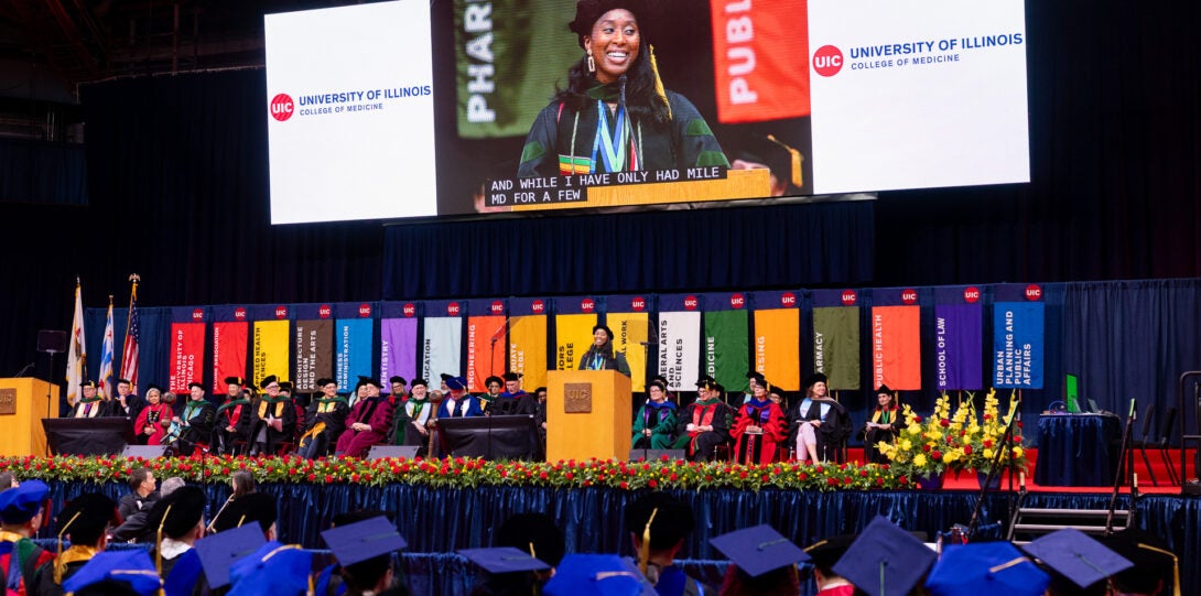 The class president speaks to graduates at the podium in front of multi-colored banners