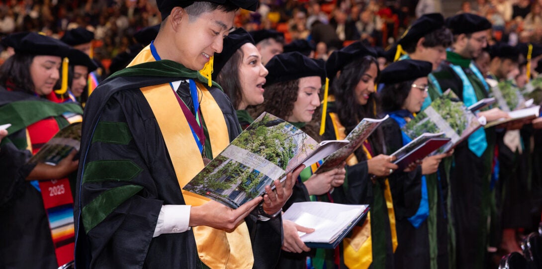 Students in graduation caps and gowns read from the ceremony programs
